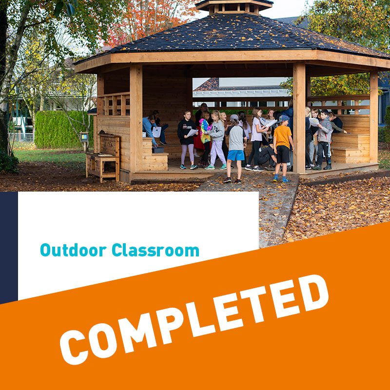 A group of students in the outdoor classroom behind the words "completed: outdoor classroom"